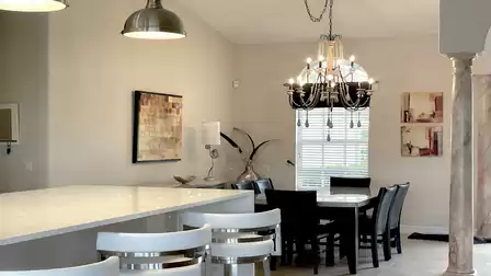 The dark furniture in the dining area provides a harmonious contrast to the white kitchen