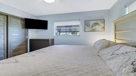Bedroom with large bed, wall mounted TV, dresser and window with blind