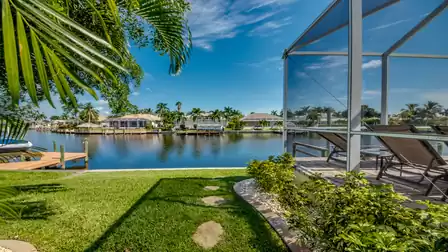 View of the tranquil canal with lush greenery in the foreground and the pool terrace of Villa Donatella on the right side of the image.