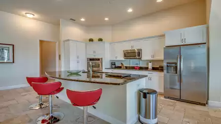 Modern kitchen with a white design, elegant granite countertop, and stylish red bar stools at the kitchen island.