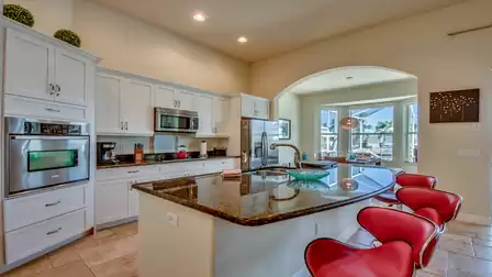 Open kitchen with high-quality stainless steel appliances, kitchen island, and direct access to the dining area with pool view.