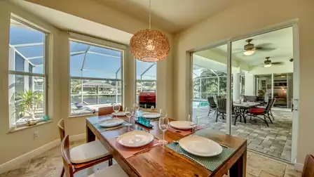 Bright dining area with an elegant wooden table, large windows, and a view of the covered terrace with pool.