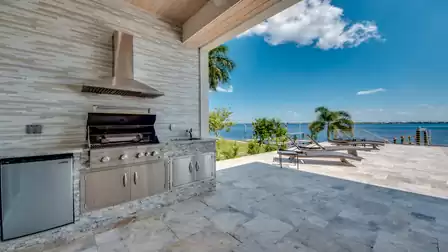 Modern outdoor kitchen with stainless steel grill, refrigerator, and river view.