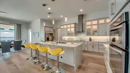 Modern kitchen with large island, yellow barstools, and stainless steel appliances.