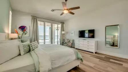 Modern bedroom with a view of the terrace and water, featuring a large bed, white furniture, and stylish decor.