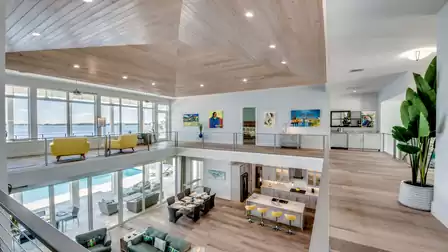 Open gallery with a wooden ceiling and large windows offering a stunning view of the pool and water; stylish interior with colorful accents.