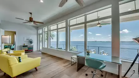 Bright workspace with desk, yellow armchairs, and floor-to-ceiling windows overlooking the water.