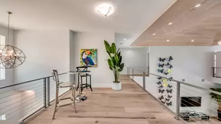Open gallery with modern bar table, plants, and artistic wall paintings, overlooking living room.