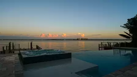 Infinity pool and raised hot tub overlooking wide river with distant buildings
