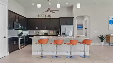 Open kitchen with dark cabinets, stainless steel appliances, and a spacious breakfast bar with leather seats.