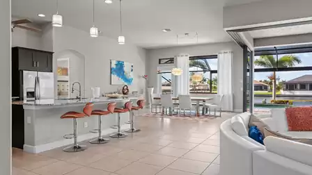 Open kitchen with a large kitchen island, modern pendant lights, and bar stools, overlooking the dining area and terrace.