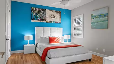 Modern guest room with a white bed, blue accent wall, and colorful artwork.