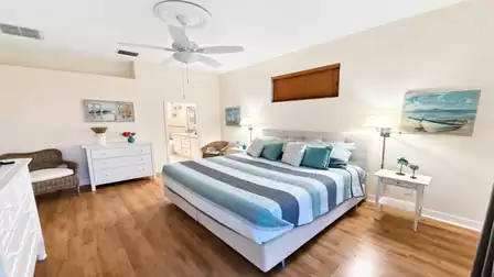 Master bedroom with striped king bed, wicker chair and doorway to ensuite bathroom