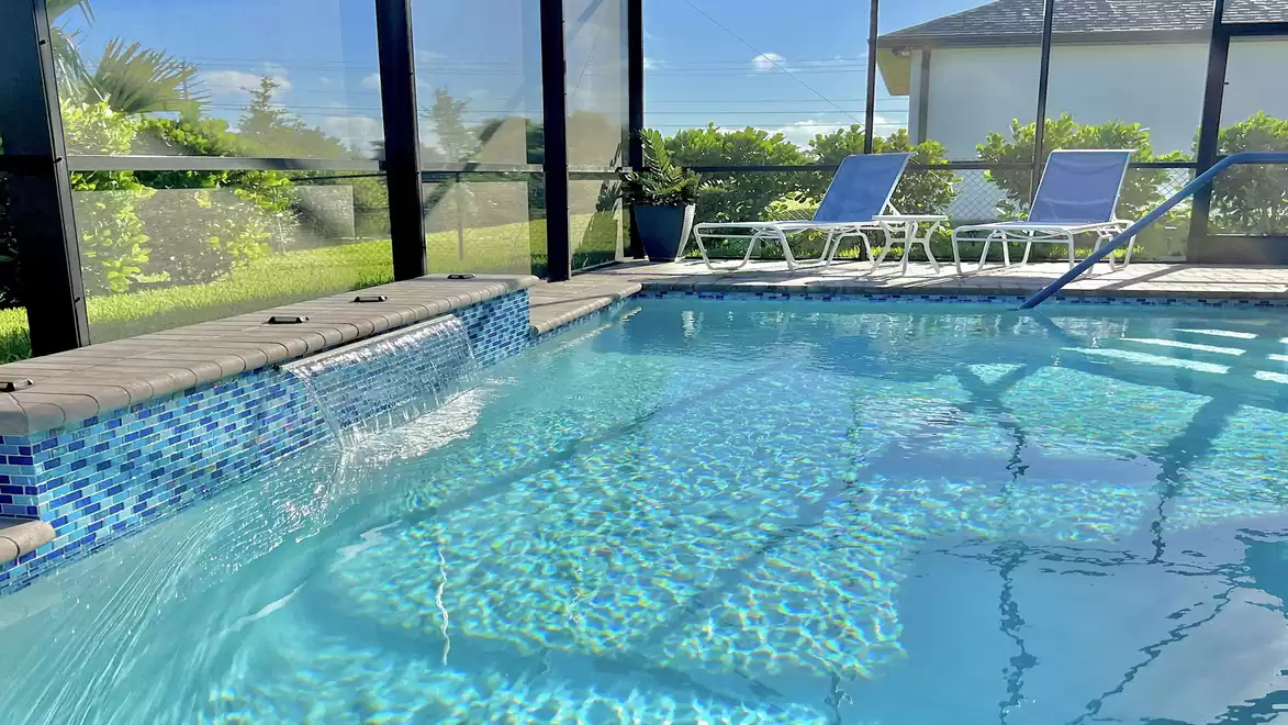 Pool with waterfall and sun loungers for relaxing moments.
