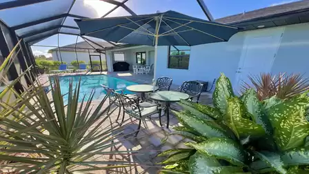Cozy seating area by the pool with umbrella and tropical plants.