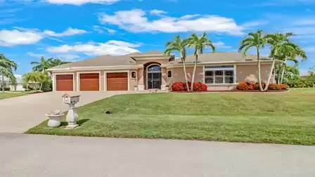 Impressive exterior view of a luxurious villa featuring three garages, a well-maintained lawn, tropical landscaping, and a majestic entrance.