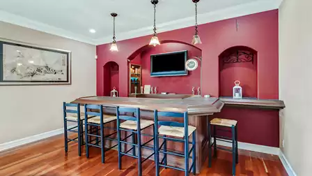 tylish home bar with an elegant counter, high chairs, and atmospheric lighting against a deep red wall. Perfect for social gatherings.