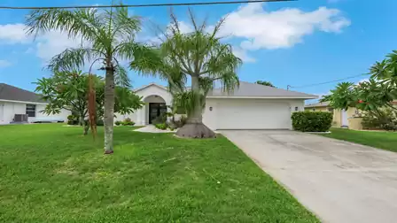 Modern villa with a two-car garage, landscaped front yard, palm trees, and tropical surroundings.