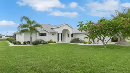 Villa Kamala in Cape Coral with a white façade, palm trees and a well-kept front garden.