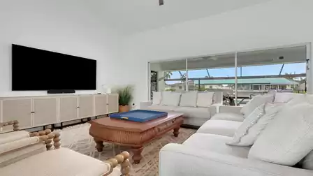Modern living room with comfortable sofas, TV, and large windows overlooking the pool patio.