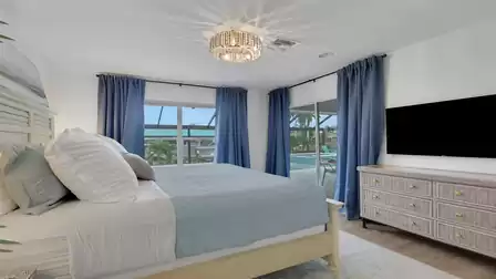 Modern bedroom with a king-size bed, smart TV, and direct access to the pool patio.