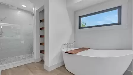 Modern bathroom with a freestanding bathtub, walk-in shower, and large window providing natural light.