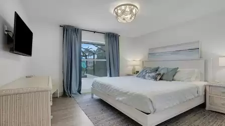 Bright bedroom with a queen-size bed, smart TV, and large window overlooking the pool.