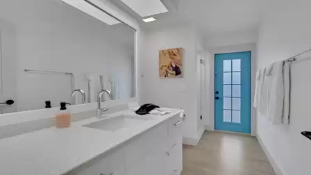 Bathroom with white vanity, large mirror, blue glass door, and wall art