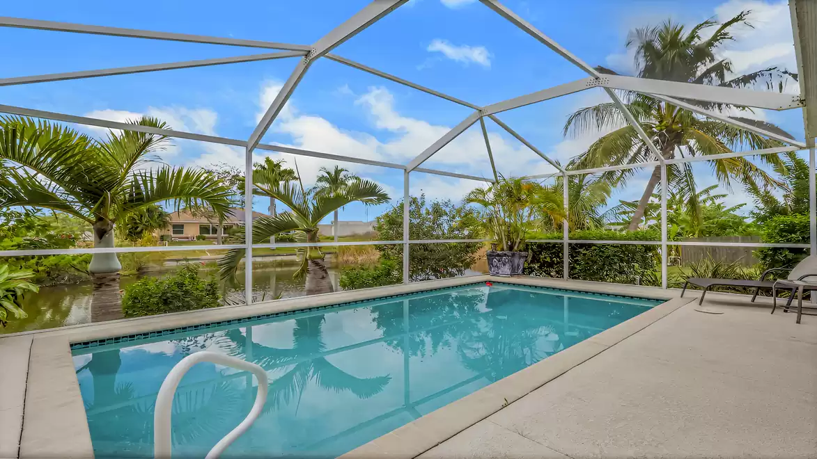 Pool with sun deck, screened enclosure, and views of palm trees and the canal.