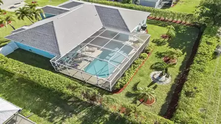 Fenced garden with palm trees and screened pool area.