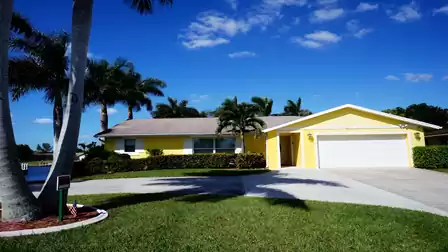 Cheerful yellow villa with manicured front yard, palm trees, and canal view in Cape Coral