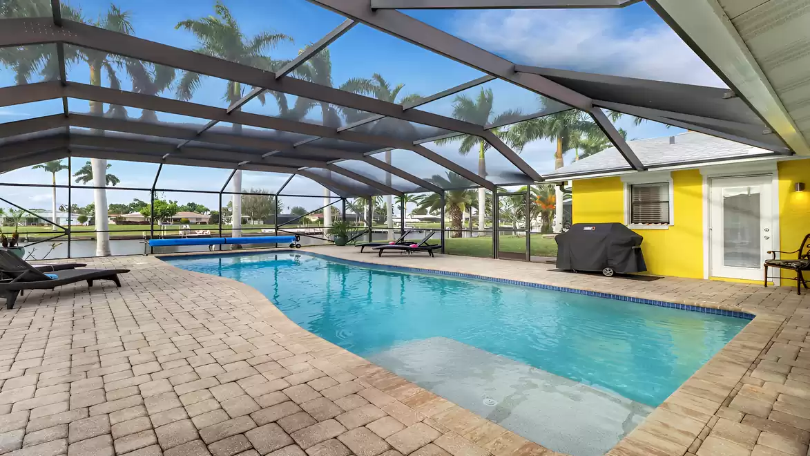 Pool area with loungers, gas grill, and screened patio by the canal - perfect for relaxing vacation days