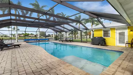 Pool area with loungers, gas grill, and screened patio by the canal - perfect for relaxing vacation days