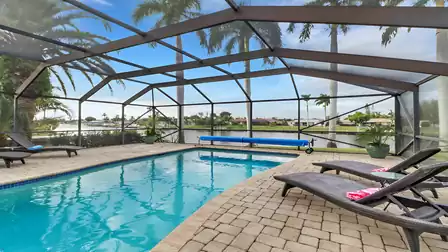 Screened-in pool area with sun loungers, canal view, and palm trees in the background.