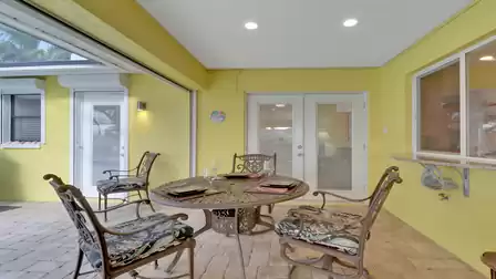 Covered outdoor dining area with four decorative chairs and round metal table, adjacent to the villa's kitchen.