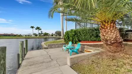 Two turquoise chairs with side table on a small platform by the canal, framed by palm trees and tropical greenery.