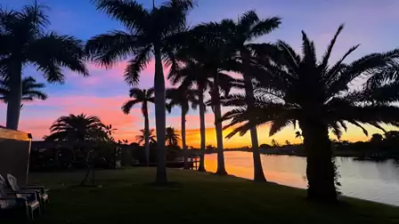 Colorful evening sky over the canal - palm trees cast long shadows as the sunset bathes the scene in romantic light.