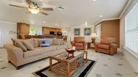Spacious living area with cozy sofa, two leather armchairs, ceiling fan, and view into the open kitchen - the ideal space to relax and gather.