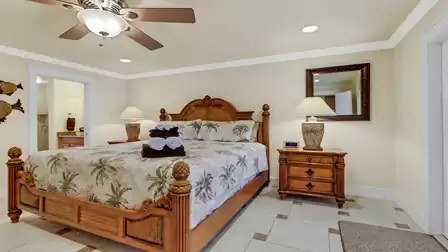 Master bedroom featuring an elegant wooden bed frame, tropical bedding, and direct access to the ensuite bathroom - a relaxing retreat with a vacation vibe.
