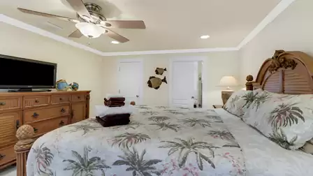 Elegantly furnished master bedroom with king-size bed, tropical palm design, and access to bathroom and closet area.