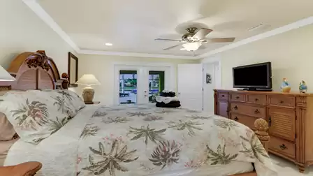 Tropical-style master bedroom with direct access to the pool area and cozy TV setup - a perfect place to wake up with water views.