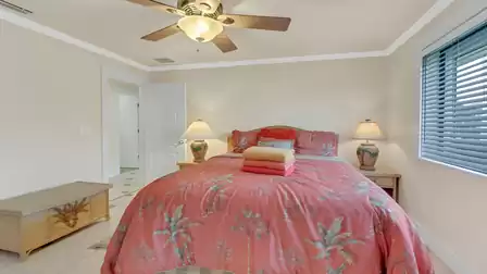 Cozy bedroom with ceiling fan, tropical red bedding, and plenty of natural light.