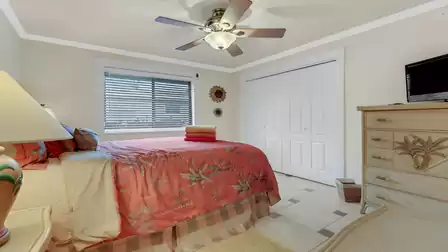 Bright bedroom with ceiling fan, large window, tropical decor, and TV chest.
