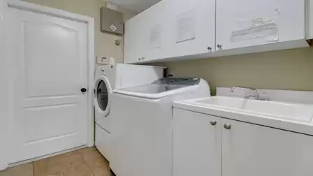 Functional laundry room featuring washer, dryer, utility sink, and white overhead cabinets