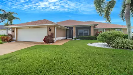 Front view of Villa Giorgio in Cape Coral with manicured lawn, palm trees, and double garage - welcoming and charming.