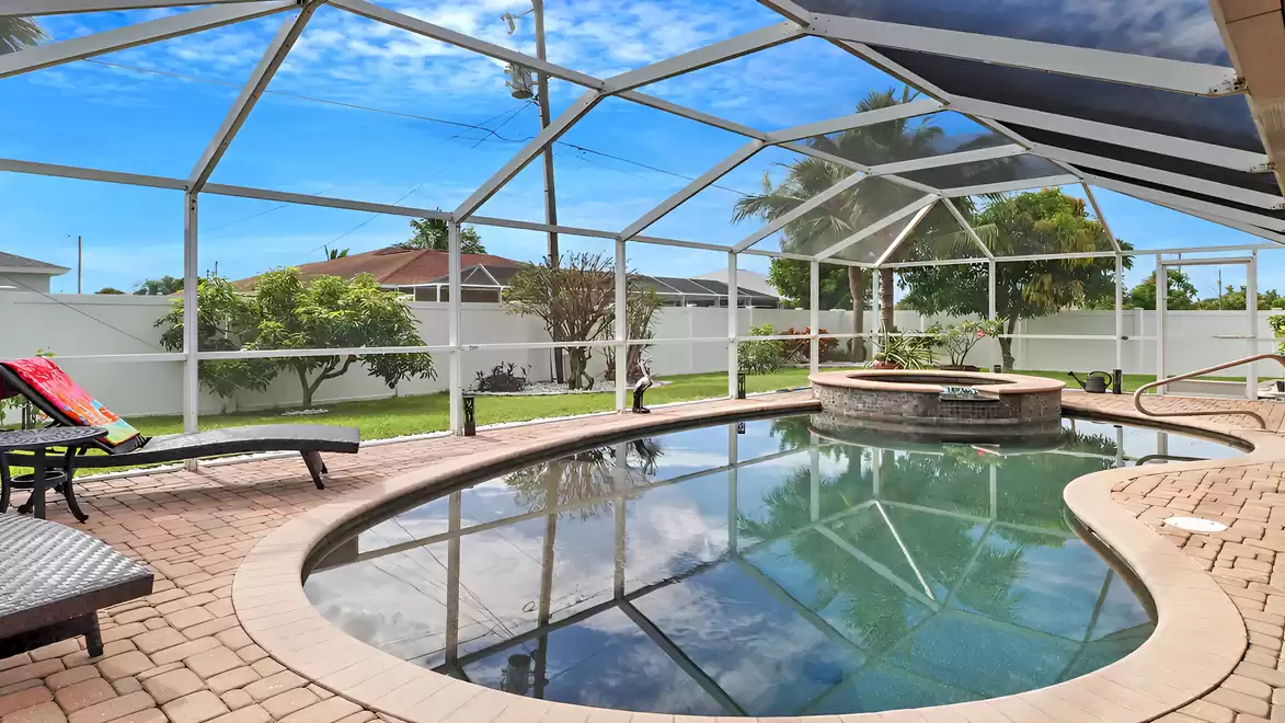 Screened-in pool area with spa, loungers, and manicured garden - ultimate relaxation under the Florida sun.