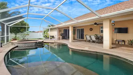 Patio with dining table and lounge area under screened enclosure overlooking pool and spa