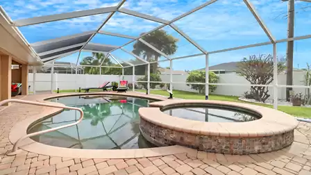 Screen-enclosed outdoor area featuring a swimming pool and built-in hot tub, surrounded by a well-kept garden with palm trees and sun loungers.