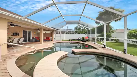 Pool area with built-in hot tub and covered dining section, enclosed by an airy screen made of aluminum posts and fine mesh.