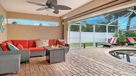 Cozy seating area with a red outdoor sofa and fire table beneath the sheltered terrace, directly by the pool area enclosed with aluminum frame and mesh screen.
